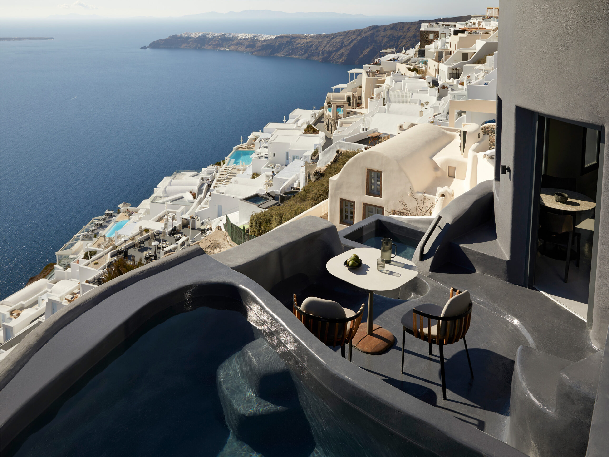 Kivotos Santorini luxury suite with private plunge pool overlooking the caldera in Imerovigli, featuring volcanic all-black architecture, curved cave-style design, panoramic sunset views, and modern five-star luxury accommodations in Santorini.