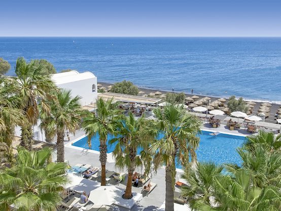 Luxury beachfront resort in Santorini with palm-lined pools, direct beach access, and contemporary five-star accommodations overlooking the Aegean Sea.